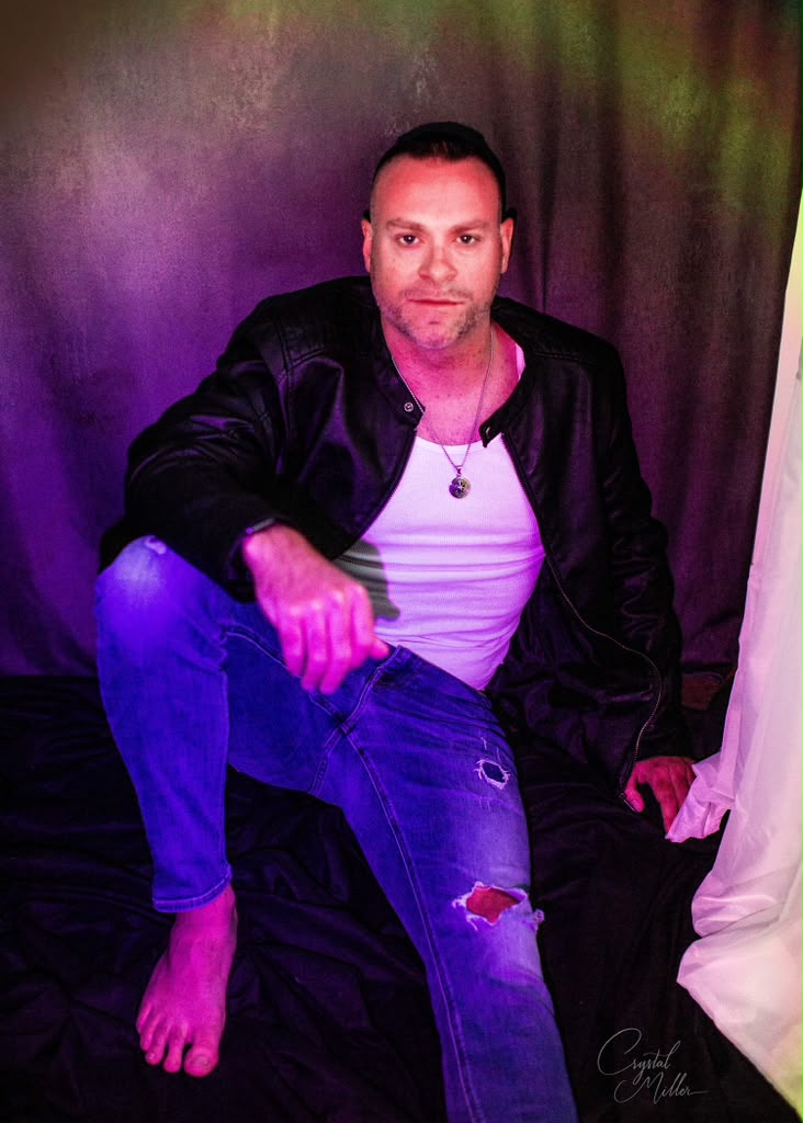 Dan Candell seated against a purple and green studio backdrop
